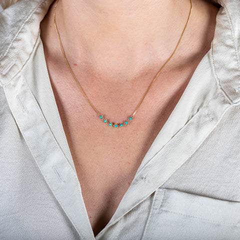 A model wears a delicate 18k yellow gold necklace with a row of woven turquoise beads in the center.