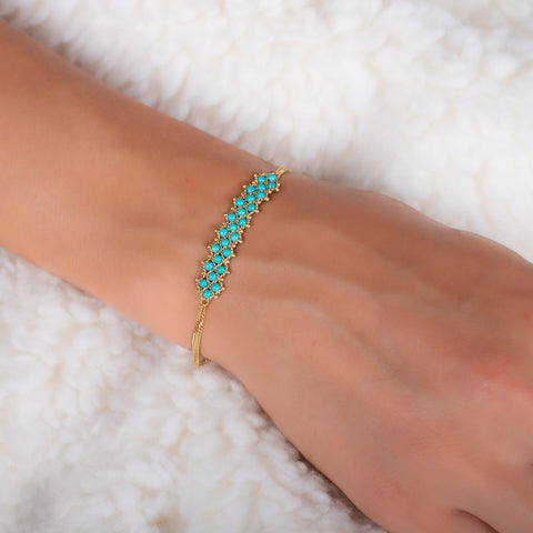 A model wears a delicate 18k yellow gold chain bracelet featuring three rows of woven turquoise beads in the center. The bracelet is finished with a lobster clasp closure.