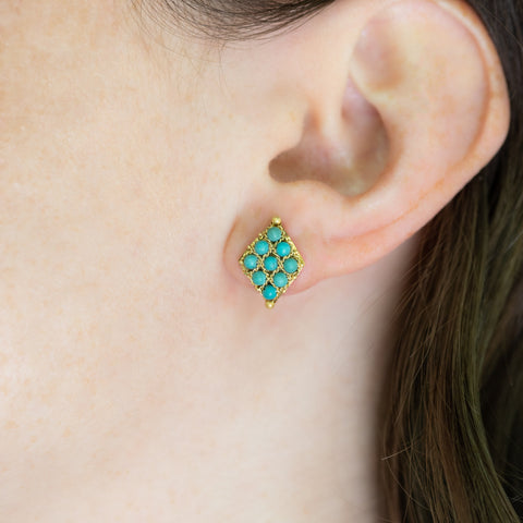 A model wears an earring crafted in 18k yellow gold chain and turquoise beads that are woven into a diamond lattice pattern and fastened with a post closure.