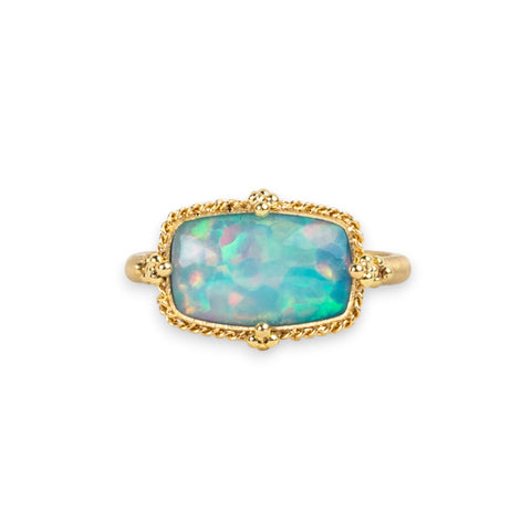Ethiopian Opal ring in 18K yellow gold, featuring an organically shaped rectangular opal shimmering with a rainbow of colors - green, orange, gold, and magenta. Meticulously handmade gold frame with braided gold and granulations.