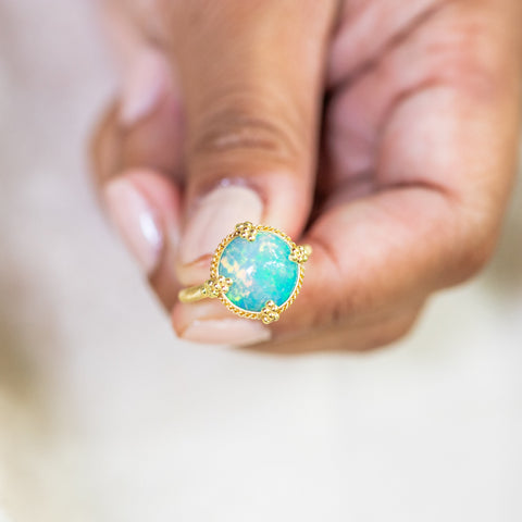 A model holds an Ethiopian Opal ring in 18K yellow gold, highlighting its bold flashes of electric green and neon yellow against sparkling turquoise. Meticulously handmade gold frame features intricate braided detail and granulated prongs. Handmade in New York