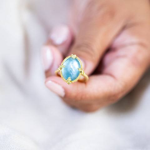 A model holds an aquamarine ring in 18K yellow gold, highlighting the dance of shades beneath the surface in the light. Handmade gold frame with braided gold accents and granulated prongs. Handmade in New York.