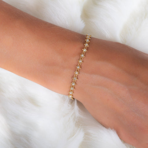 A model wears an 18k yellow gold bracelet that features silver diamond beads woven throughout a delicate chain.
