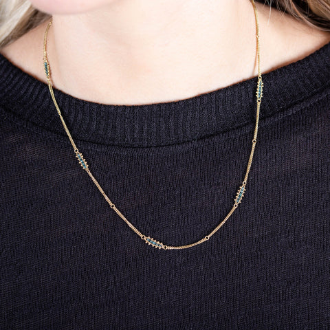 A model wears an 18k yellow gold chain necklace with rows of blue diamond stations woven throughout.