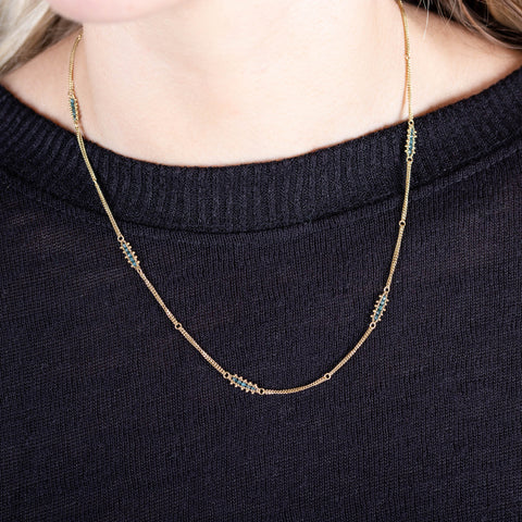 A model wears an 18k yellow gold chain necklace with rows of blue diamond stations woven throughout. 