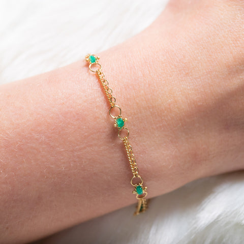 A close up of a delicate 18k yellow gold chain bracelet that is dotted with emerald bead stations throughout.