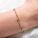 A close up of a delicate 18k yellow gold chain bracelet that is dotted with emerald bead stations throughout.