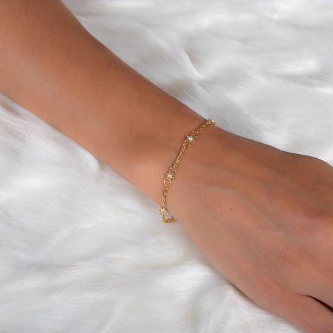A model wears a delicate 18k yellow gold chain bracelet that is dotted with pearl beads throughout. The bracelet is finished with a lobster clasp closure.