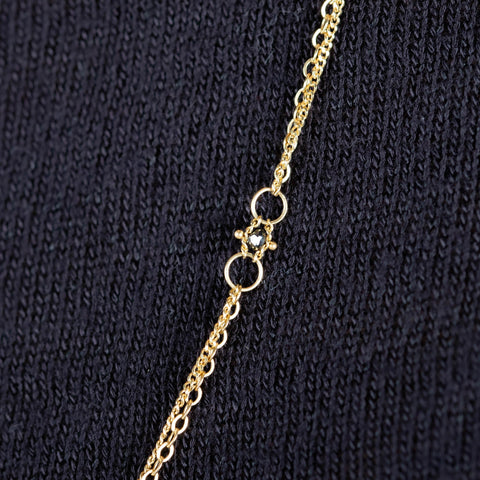 A close-up of a delicate woven 18k yellow gold chain necklace with a black diamond bead station.