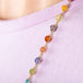 A close-up of a multi-colored woven gemstone necklace featuring Sunstone, Peridot, Aquamarine, Lolite, Apatite, Imperial Topaz, Rhodolite Garnet, Morganite, Tanzanite, Amethyst, and Grossular Garnet