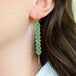 A close up of a pair of long turquoise earrings which feature a woven lattice pattern and two dangling chains at the bottom of the earring.