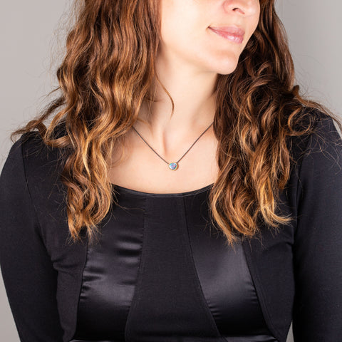 A model wears a small oval shaped Australian opal pendant set in 18k yellow gold on an oxidized sterling silver chain.