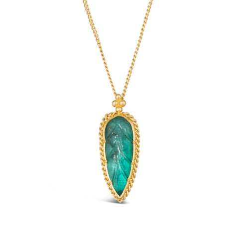 An elongated carved leaf shaped emerald pendant is set in 18k yellow gold with a braided detail and hangs on a delicate chain.