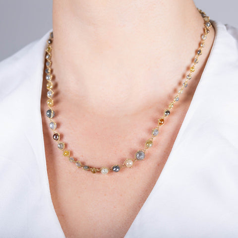 A model wearing a multi-colored diamond necklace that features diamonds in a variety of colors strung on an 18k yellow gold chain necklace.