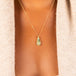 An elongated teardrop shaped opal pendant is wrapped in an 18k yellow gold bezel with four beaded prongs on a delicate chain