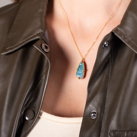 A large blue and green teardrop shaped opal is set in 18k yellow gold and hangs on a delicate chain.