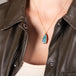 A large blue and green teardrop shaped opal is set in 18k yellow gold and hangs on a delicate chain.