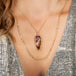 A model wears a large teardrop shaped tourmaline with a floral carving. The pendant is set in an 18k yellow gold chain wrapped bezel and hangs on a delicate chain.