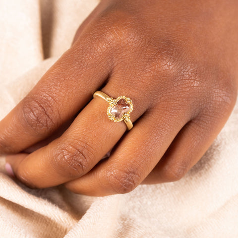 A model wears a small rectangular champagne diamond set in an 18k yellow gold bezel wrapped in a chain with four granulated prongs on a thin band.