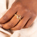 A model wears a small rectangular champagne diamond set in an 18k yellow gold bezel wrapped in a chain with four granulated prongs on a thin band.