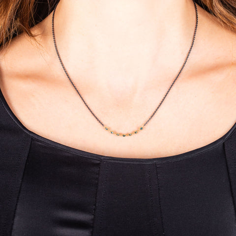 A row of blue diamonds is wrapped in 18k yellow gold bezels and set in an oxidized sterling silver chain.