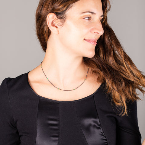 A model wears a short emerald station necklace with 18k yellow gold bezels and set throughout an oxidized sterling silver chain.