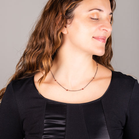 A model wears a short rubies station necklace with 18k yellow gold bezels and set throughout an oxidized sterling silver chain.