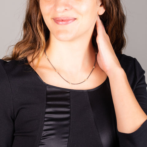 A model wears a short silver diamond station necklace with 18k yellow gold bezels and set throughout an oxidized sterling silver chain.