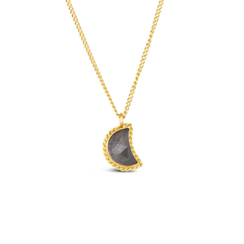 A small charcoal colored diamond cut in the shape of a crescent is set in an 18k yellow gold chain wrapped bezel. The pendant hangs on a delicate chain.
