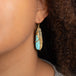 A model wears a large turquoise teardrop shaped earring. The stone is wrapped in an 18k yellow gold chain with blue diamonds set in the chain.