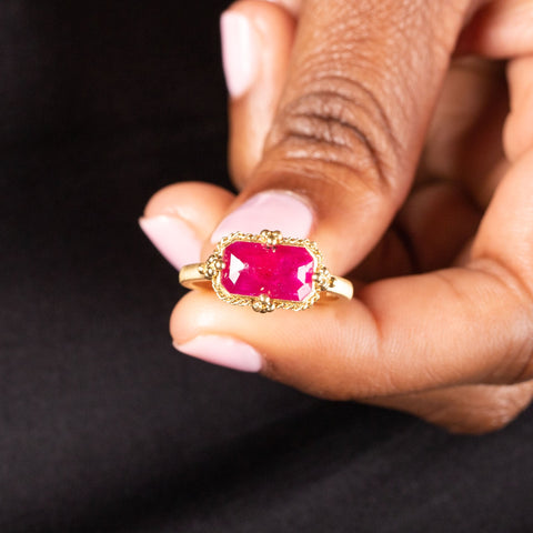 A model holds a faceted ruby ring with a braided bezel and four granulated prongs on a thin 18k yellow gold band.