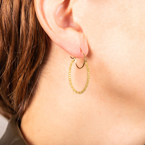 A model wears a diamond cut chain hoop crafted in 18k yellow gold. The hoop has a glittering stardust like effect. 