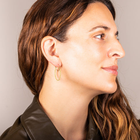 A model wears a medium 18k yellow gold diamond cut chain hoop earring that has a glittering stardust like effect.
