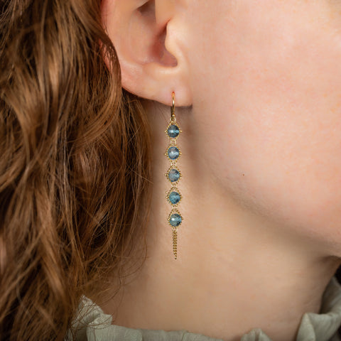 A model wears a long blue topaz earring suspended in 18k yellow gold chain.