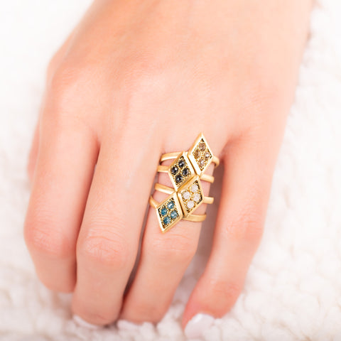 A model wears a stack of four mini textile rings crafted in 18k yellow gold with blue diamonds, silver diamonds, black diamonds and Champagne diamonds.