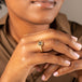 A model wears a small hexagon shaped charcoal diamond ring set in 18k yellow gold with a chain wrapped bezel.