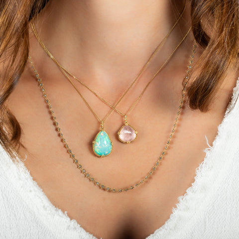 A model wears a teardrop shaped morganite pendant layered with a teardrop shaped opal pendant and silver diamond chain.