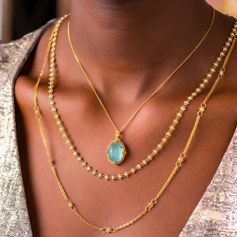 A model wears three layered necklaces, including a large aquamarine pendant, a pearl chain and a champagne diamond chain necklace.