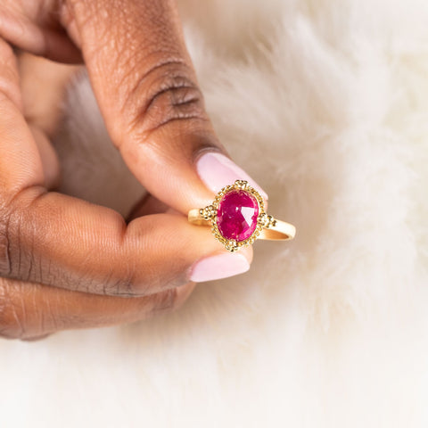 A model holds a small faceted oval shaped ruby ring with an 18k yellow gold bezel on a thin band.
