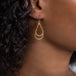 A model wears a large 18k yellow gold interlocking teardrop hoop earring.