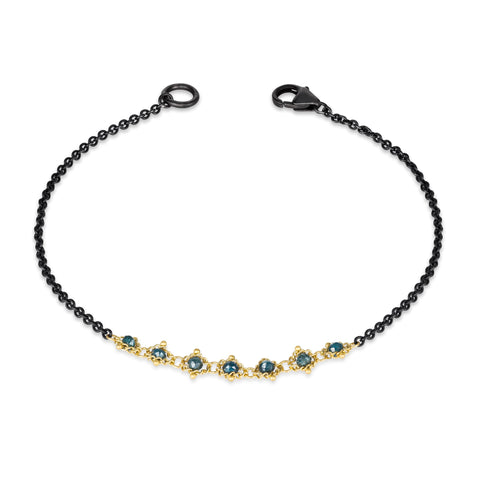 This oxidized sterling silver bracelet features a row of blue diamonds suspended in 18k yellow gold chain in the center.