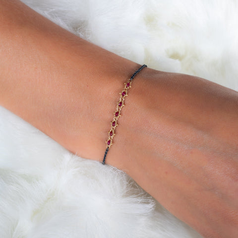 This oxidized sterling silver bracelet features a row of red rubies suspended in 18k yellow gold chain in the center.