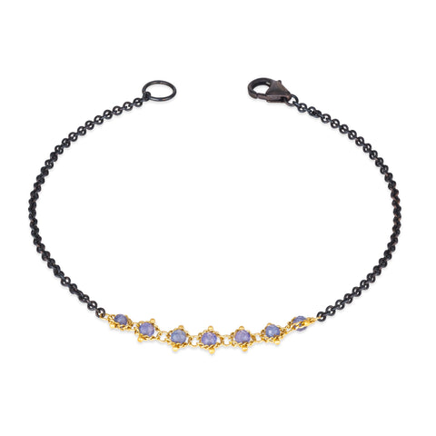 This oxidized sterling silver bracelet features a row of blue tanzanite suspended in 18k yellow gold chain in the center.