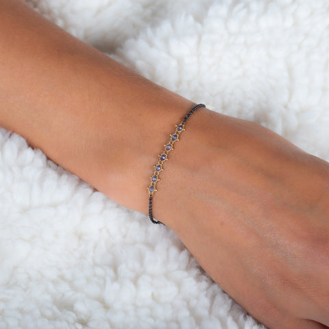 This oxidized sterling silver bracelet features a row of blue tanzanite suspended in 18k yellow gold chain in the center.