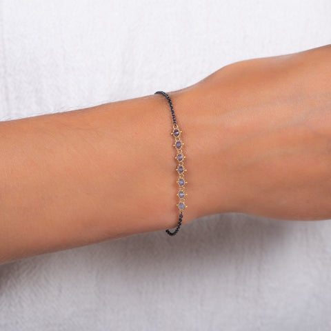 This oxidized sterling silver bracelet features a row of blue tanzanite suspended in 18k yellow gold chain in the center.