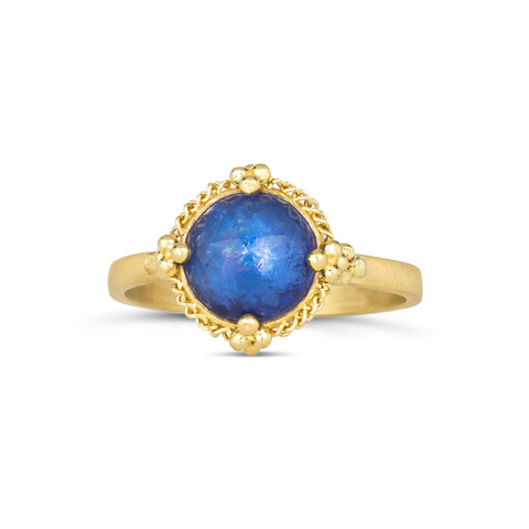 A round faceted tanzanite stone is set in 18k yellow gold with a braided detail around the bezel and four granulated prongs.