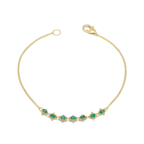 This delicate 18k yellow gold chain bracelet features a row of woven green emeralds in the center and closes with a lobster clasp.