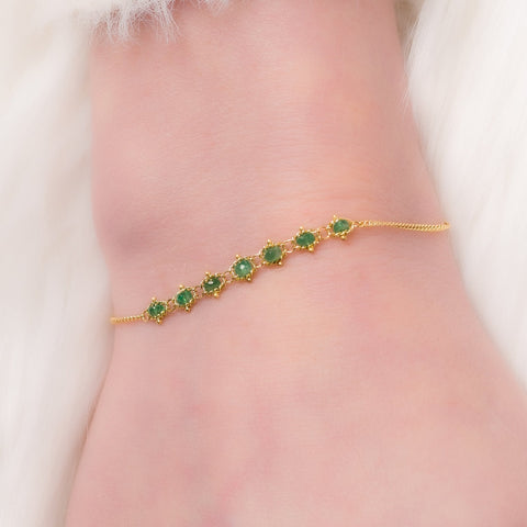 This delicate 18k yellow gold chain bracelet features a row of woven green emeralds in the center and closes with a lobster clasp.