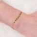 This delicate 18k yellow gold chain bracelet features a row of woven green emeralds in the center and closes with a lobster clasp.
