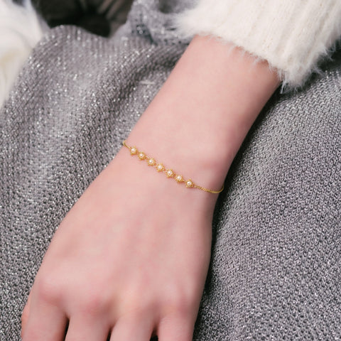 This delicate 18k yellow gold chain bracelet features a row of woven pearls in the center and closes with a lobster clasp.